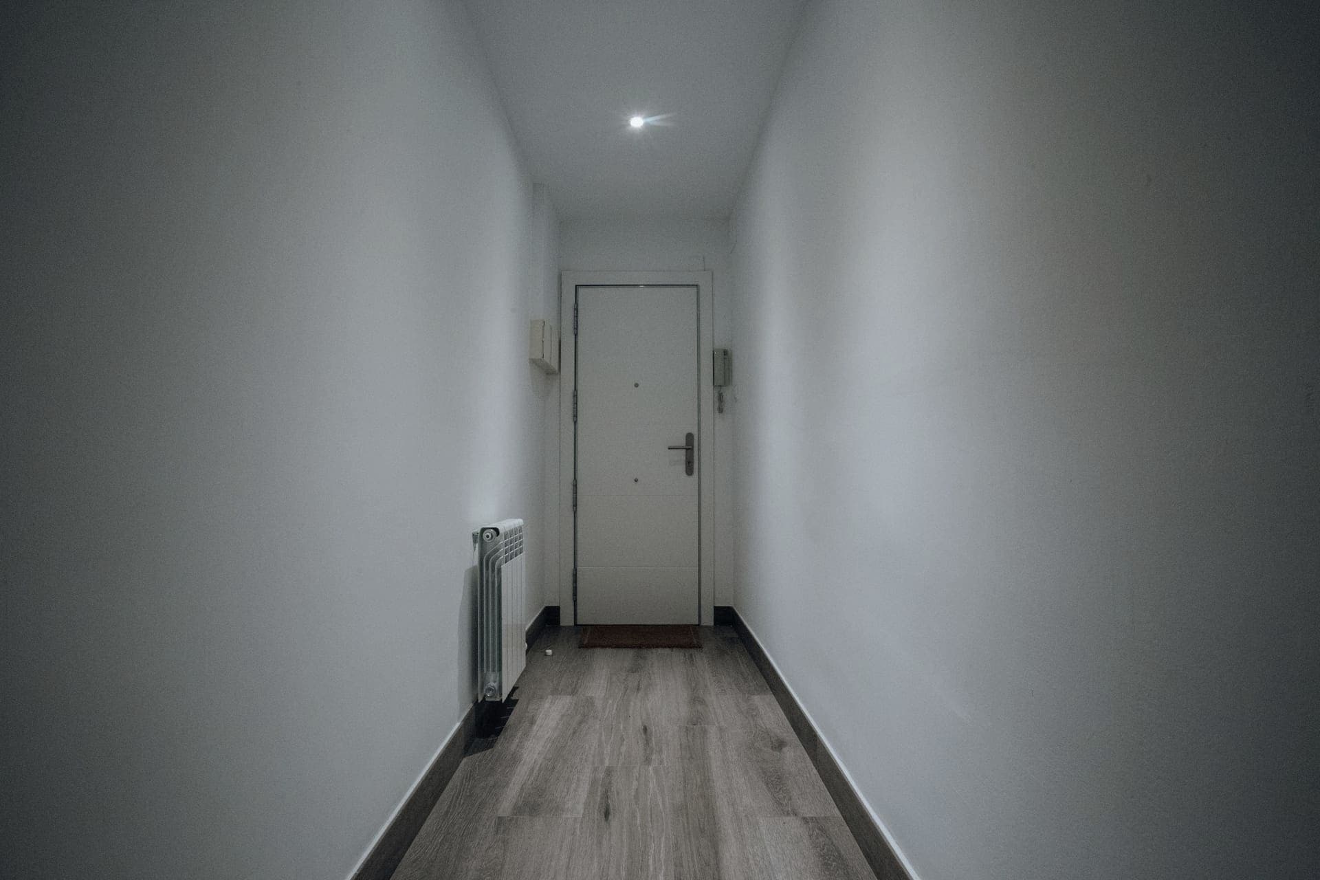 An empty hallway with a wooden floor and an open doorway, the kind of transition a robot vacuum has to cross